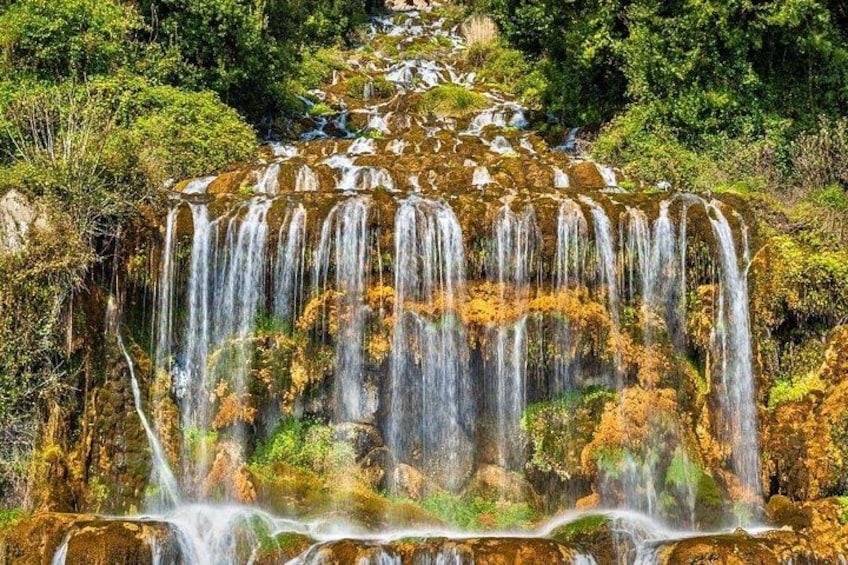 A multi-tiered waterfall cascading through a forested area. 1