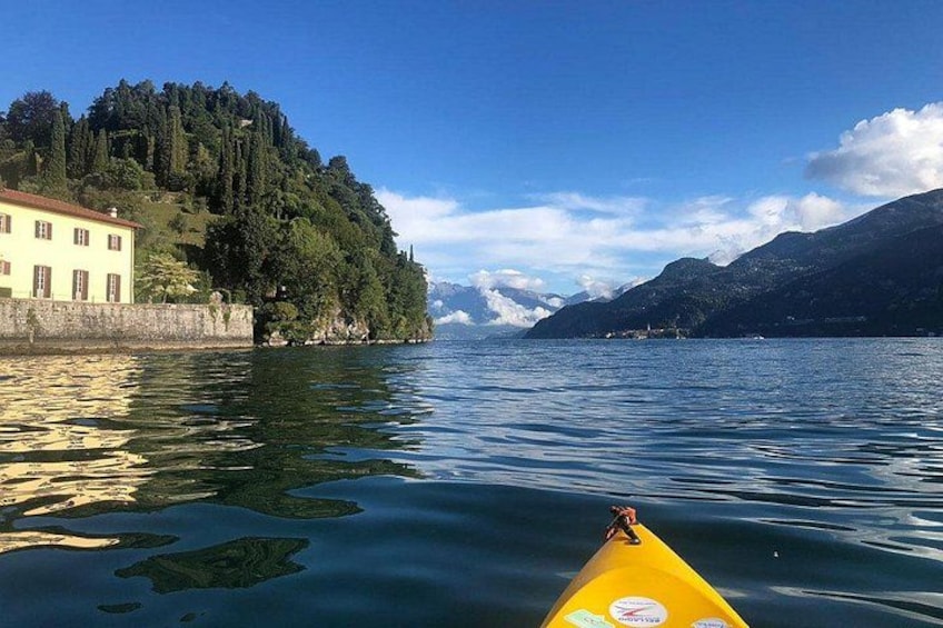 Un lago tranquilo con un kayak amarillo, un edificio a la izquierda y montañas al fondo. 3