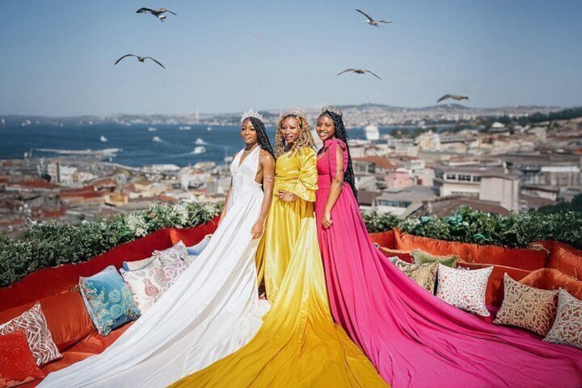 Three women in colorful dresses standing on a red couch with a cityscape in the background. 3