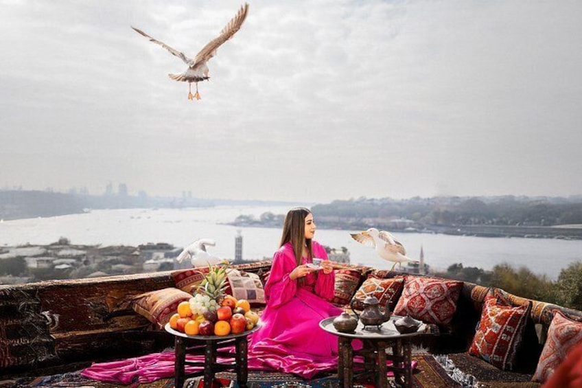 A person in a pink dress sitting on a couch with a table of fruits and a bird on the table. 2