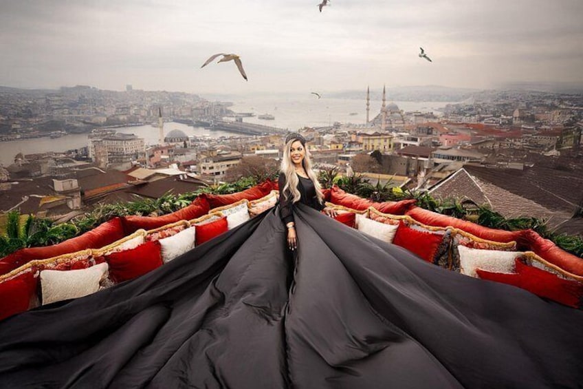 A person in a long black dress standing on a rooftop with a view of a cityscape, including a prominent tower and a river. 4