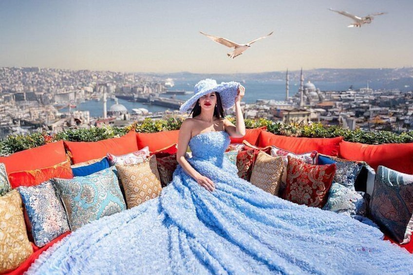 A person in a blue dress sitting on a red and blue patterned sofa with a cityscape in the background. 5