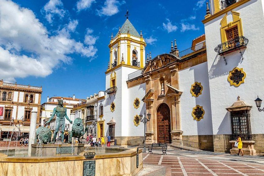 A plaza with a fountain, a statue, and a building with a bell tower. 1