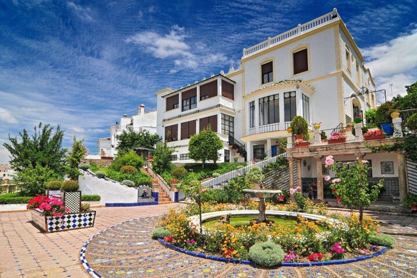 A multi-story building with a white facade, surrounded by a landscaped garden with various plants and flowers. 2