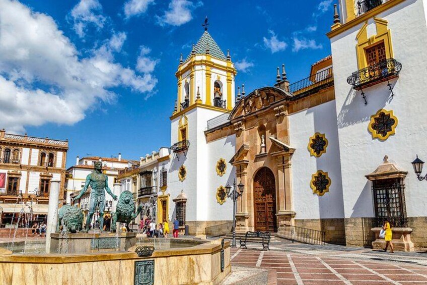 A plaza with a fountain, a statue, and a church with distinctive yellow and white architecture. 1