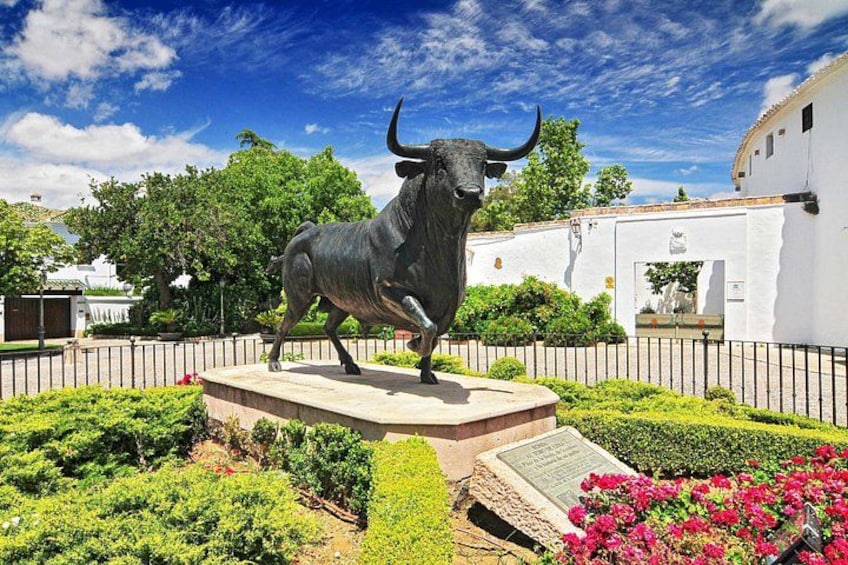 A bull statue in a garden with white buildings in the background. 2