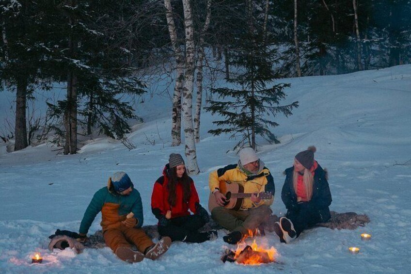 Four people sitting on the snow with a fire between them. 3