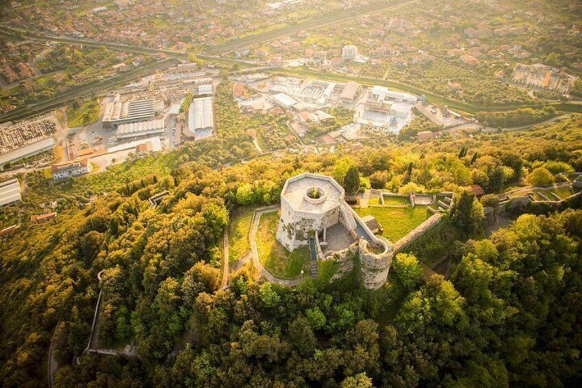 Luchtbeeld van een historisch kasteel, omringd door dicht bos, met moderne gebouwen op de achtergrond. 5