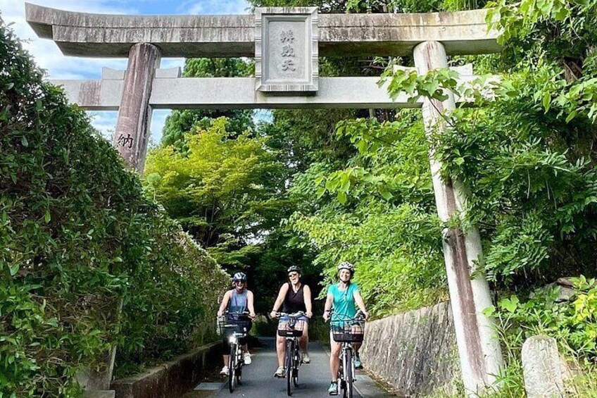 Three cyclists on a path under a stone bridge with greenery on either side. 1