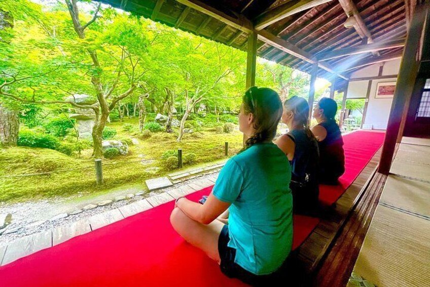 People sitting on a red mat in a covered area with a view of a garden. 3