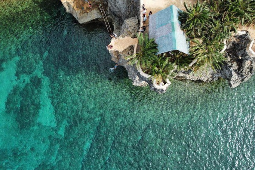 Un paisaje costero con aguas turquesas cristalinas, un promontorio rocoso y algunas personas cerca de la playa. 2