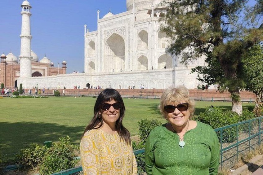 Two people standing in front of the Taj Mahal with a clear view of the monument and a green lawn. 4