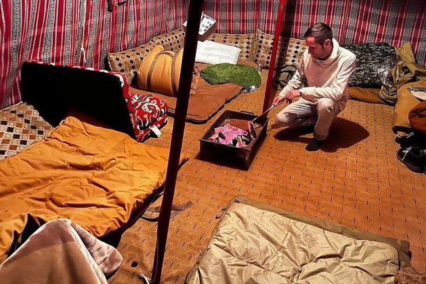 A person sitting on a bed in a tent-like structure with patterned curtains and a woven floor. 5