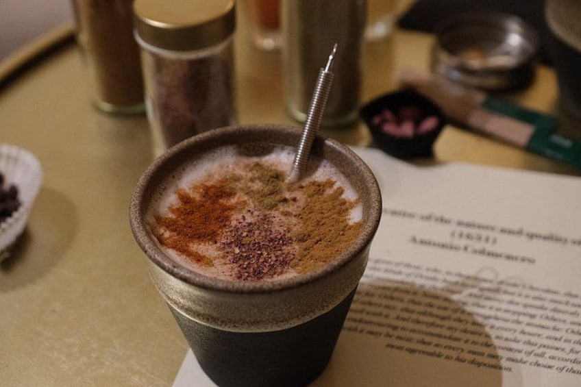 Een kop koffie met een metalen rietje, een beetje kaneel erover en een menukaart op de achtergrond. 1