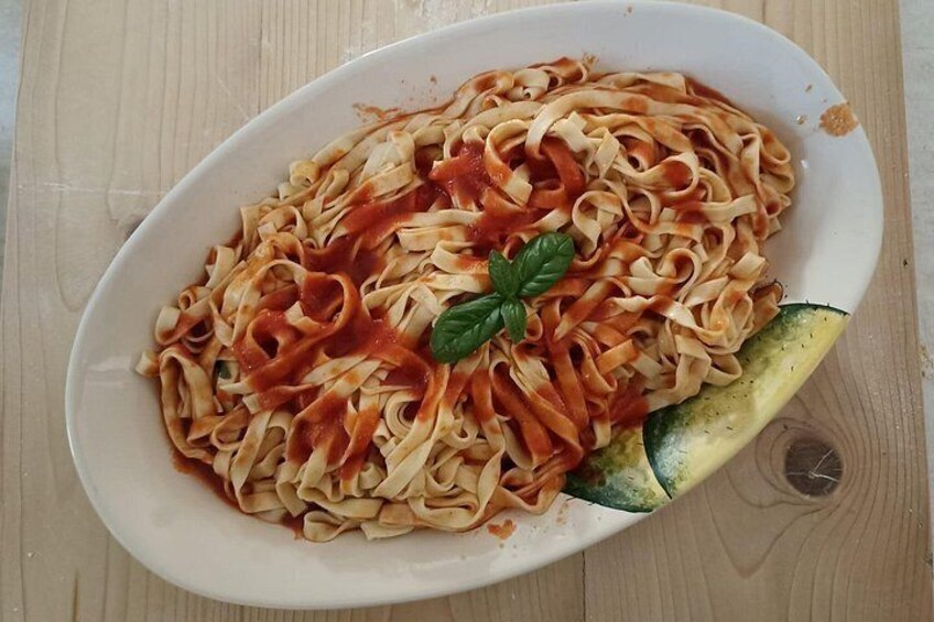 A plate of pasta with tomato sauce, garnished with a basil leaf, and a slice of zucchini on the side. 3