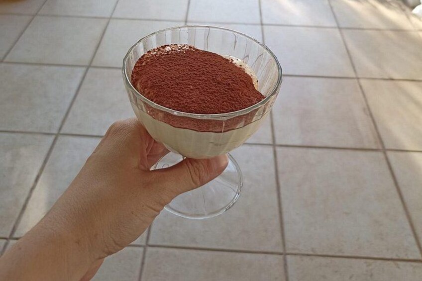 A hand holding a glass bowl containing a dessert with a red powder on top. 4