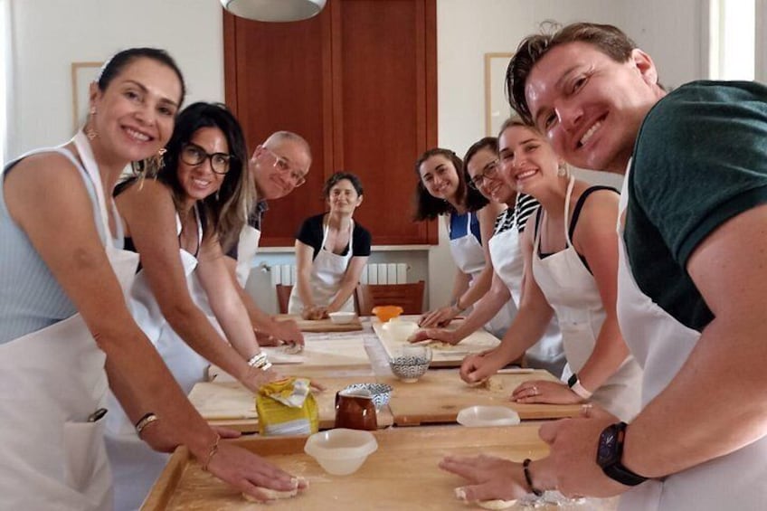 A group of people wearing aprons, engaged in a cooking activity around a wooden table. 1