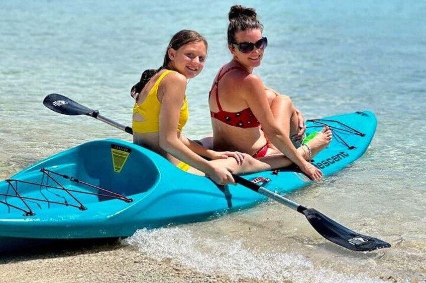 Dos personas en un kayak azul sobre una playa arenosa con agua. 2