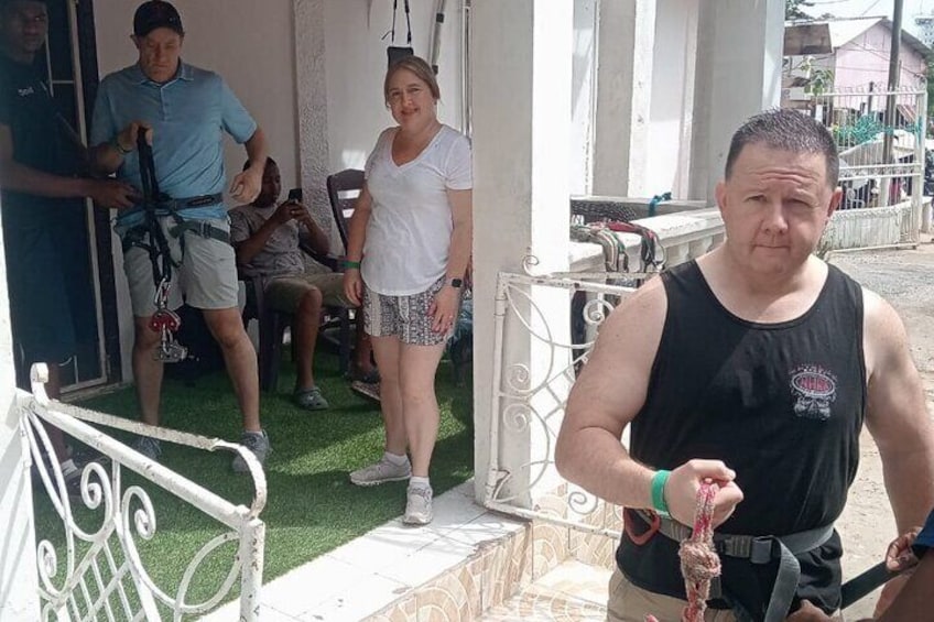 A man in a black tank top and shorts, a woman in a white top and patterned shorts, and another man in a blue shirt and shorts standing near a white railing. 5