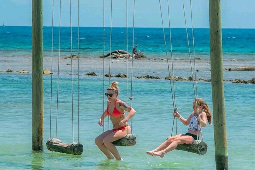 Three people on swings over a body of water with a beach and rocks in the background. 2
