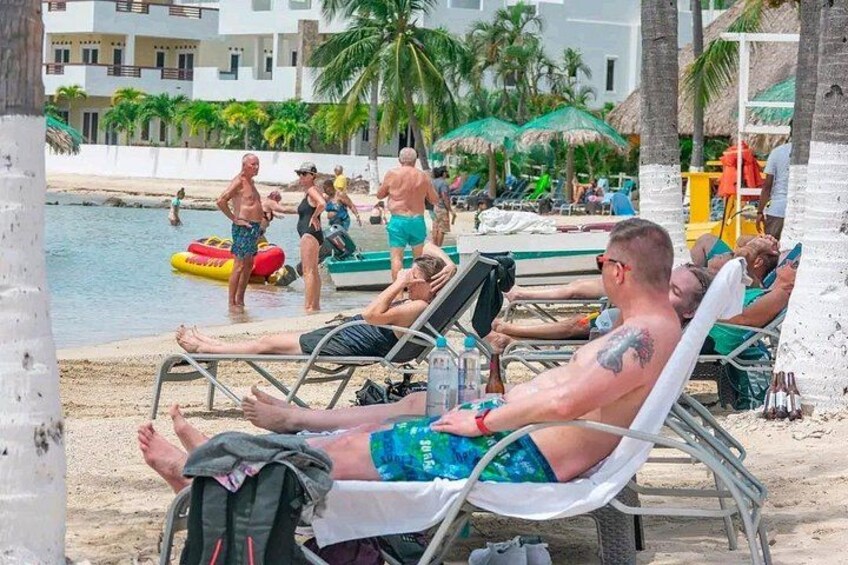 A beach with people sunbathing, a pool, and palm trees. 2