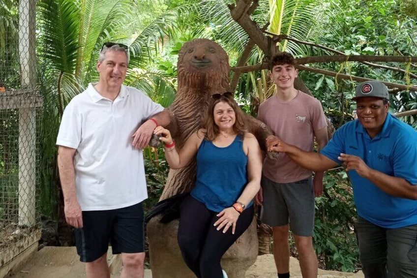 A group of people posing with a large animal, possibly a sea turtle, in a fenced enclosure with tropical vegetation. 2