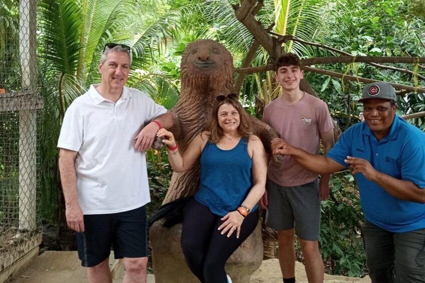 A group of people posing with a large animal in a fenced enclosure with tropical vegetation. 2