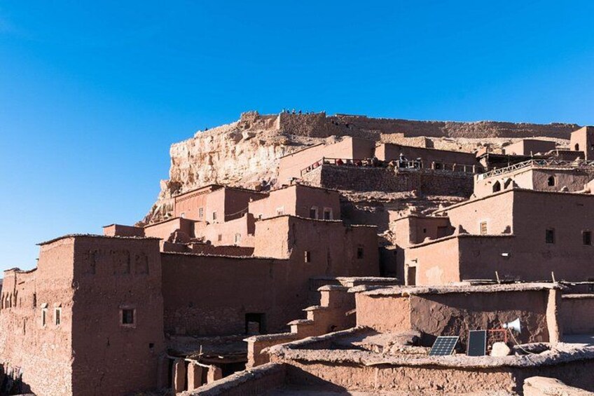 A historic adobe village with terraced structures and a prominent fortress-like building on a hill. 2