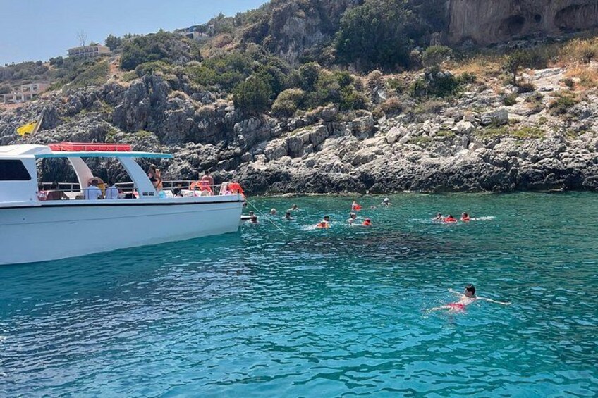 A boat with people swimming in the water, rocky cliffs in the background, and clear blue water. 3