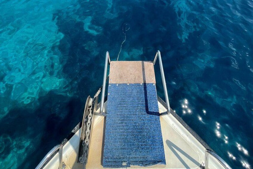 A boat's deck with a blue mat, metal railings, and clear blue water. 4