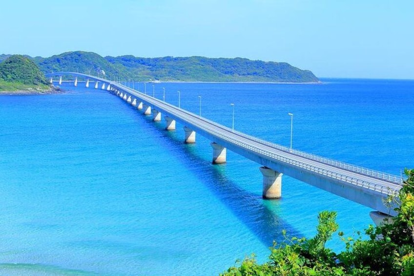 A long bridge over a blue body of water with mountains in the background. 3