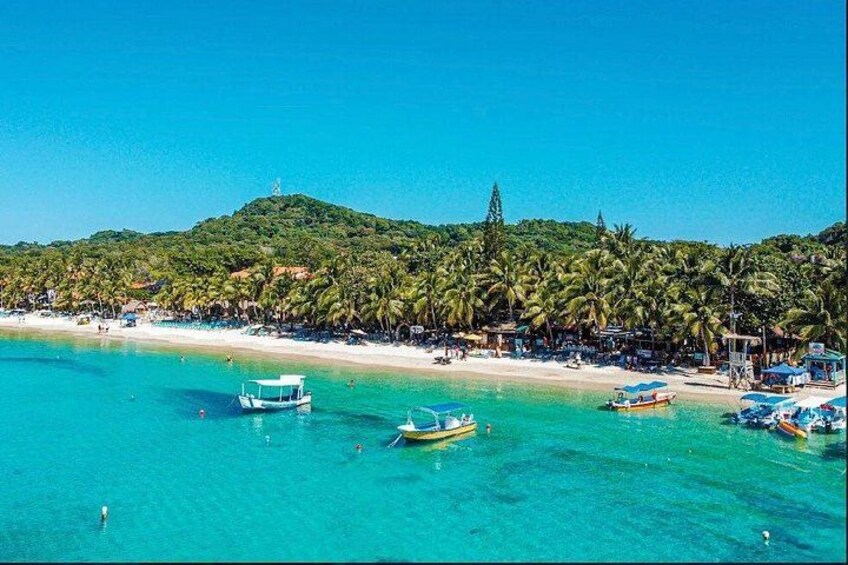 Een strand met helder turquoise water, boten en palmbomen. 1