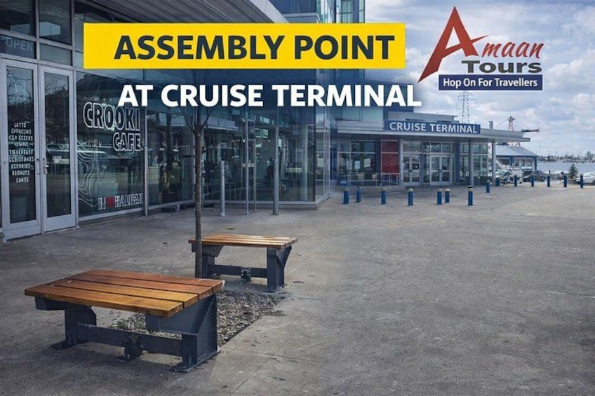 A cruise terminal with an assembly point marked by a yellow sign, a Crooki Cafe, and a wooden bench. 3