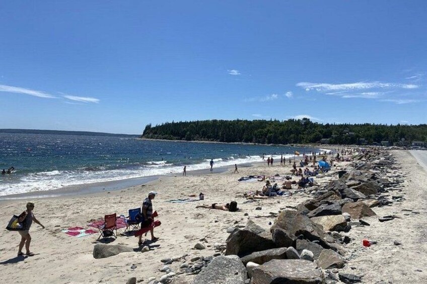 A beach with people sunbathing, chairs, and rocks. 5