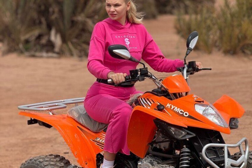 Iemand in roze rijdt op een oranje Kymco quad in een woestijnachtige omgeving. 2