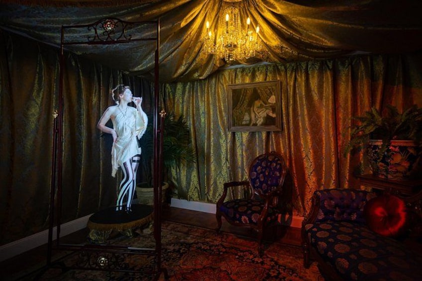 A room with a mannequin in a dress, a chandelier, and patterned curtains. 2