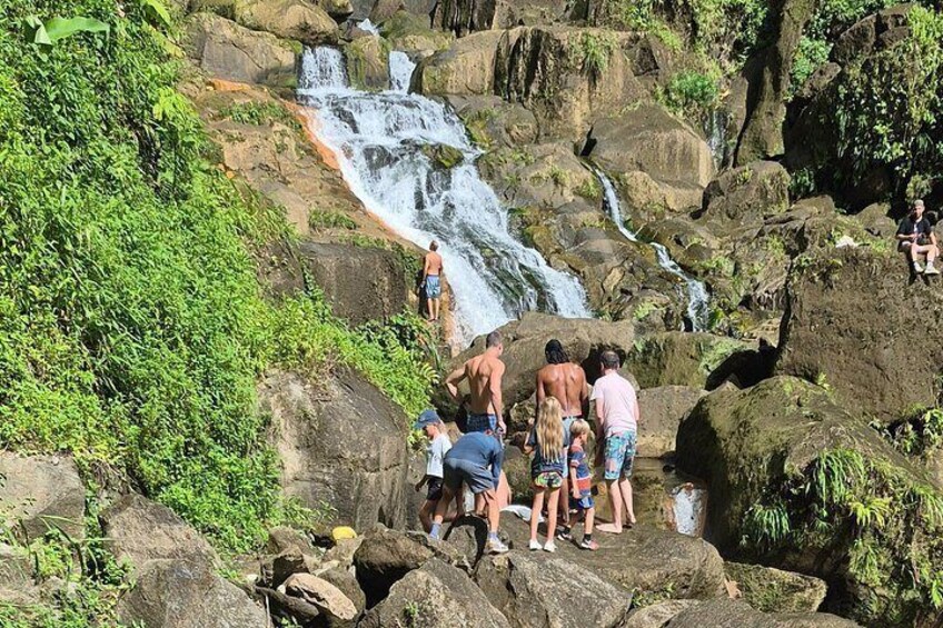 Ein Wasserfall stürzt über Felsen, umgeben von stehenden und sitzenden Personen. 3