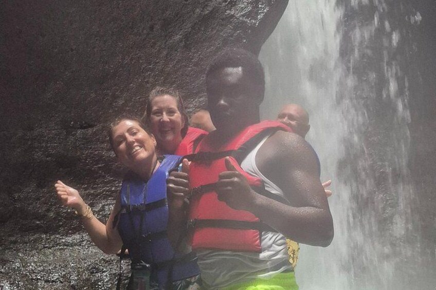 A person in a red life jacket and another in a blue life jacket standing near a waterfall. 4