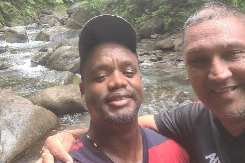 Two people near a flowing stream with rocks and greenery in the background. 4