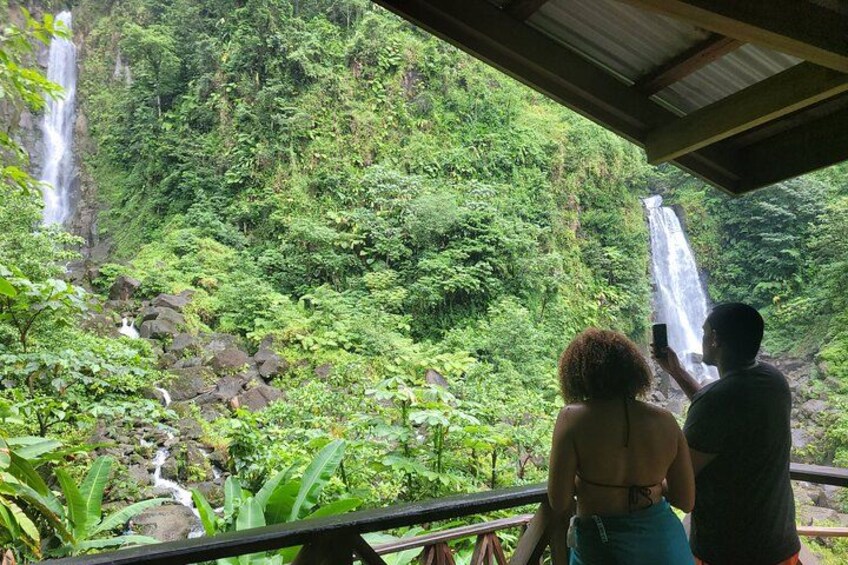A couple taking a photo of a waterfall in a lush, green forest. 1