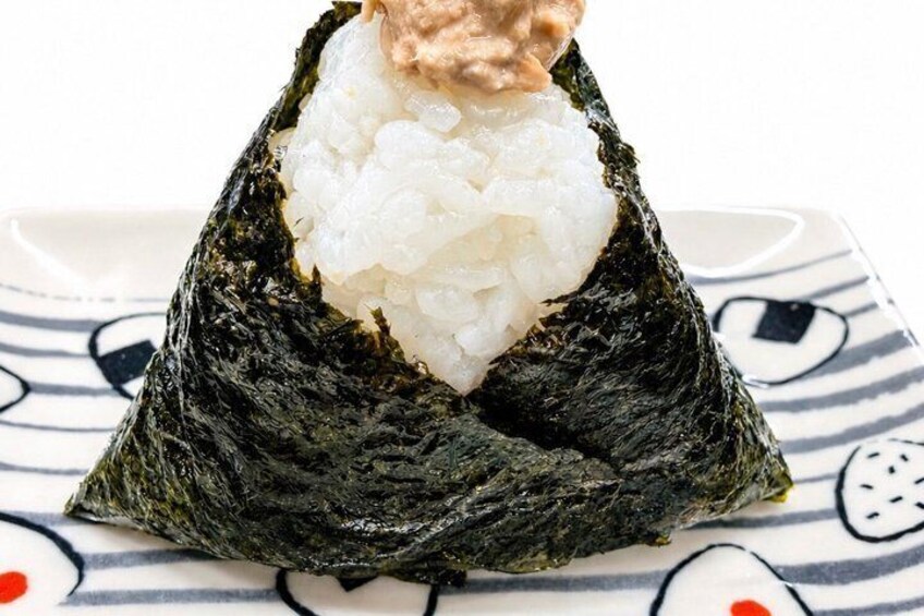 A sushi rice mound topped with a pinkish topping, wrapped in seaweed, on a patterned plate. 4