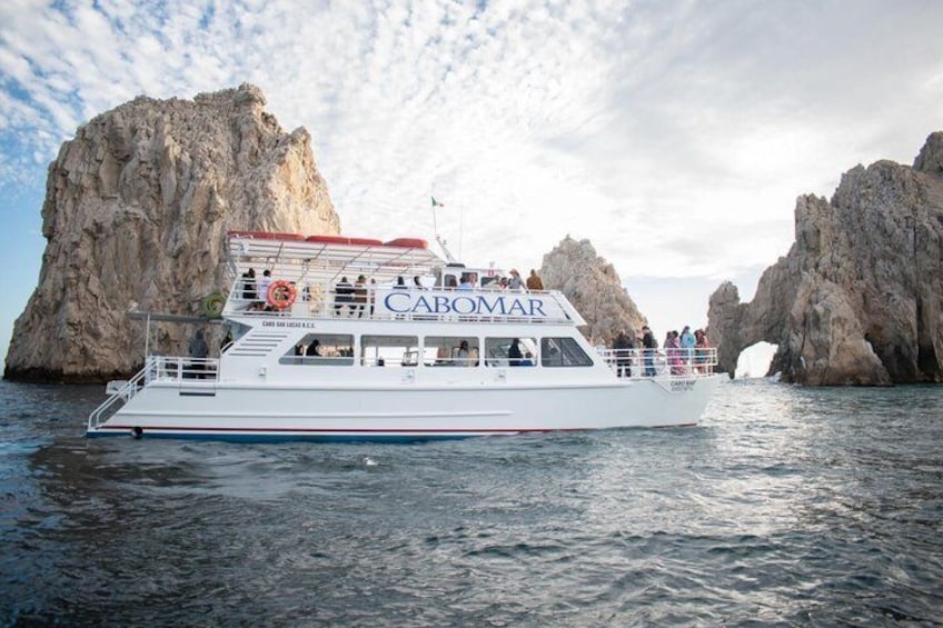 Un barco blanco llamado CABOMAR con pasajeros navegando cerca de acantilados rocosos. 3