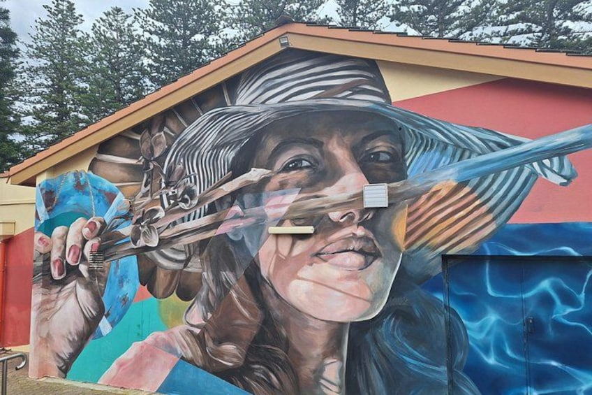 A mural with a person holding a paintbrush, trees in the background, and a building with a sloped roof. 4