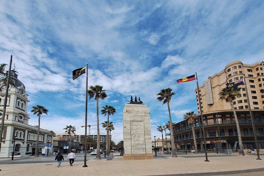 A plaza with a central monument, palm trees, and buildings with flags. 3