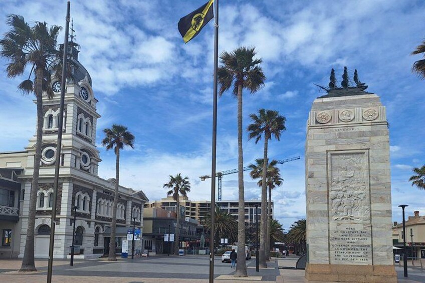 A historic building with a clock tower, palm trees, and a monument with inscriptions. 5