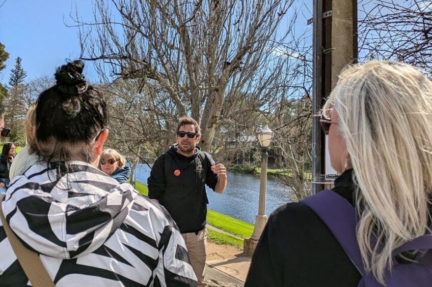 A group of people outdoors near a body of water, with trees and a lamp post in the background. 2