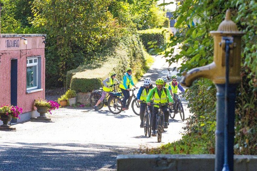 A group of cyclists on a road with a building labeled 'Coca-Cola' and a lamppost. 1