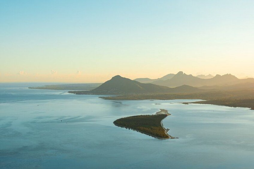 Eine Küstenlandschaft mit einer markanten Bergkette im Hintergrund, ruhigem Meer und einer kleinen Insel mit geschwungener Küstenlinie. 2