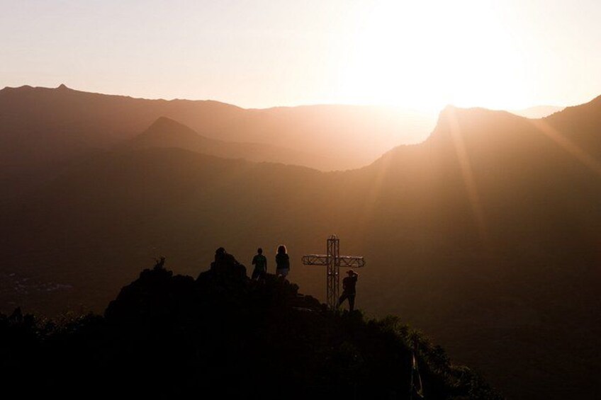 Ein Kreuz auf einem Berggipfel, im Hintergrund ein Sonnenuntergang. 1