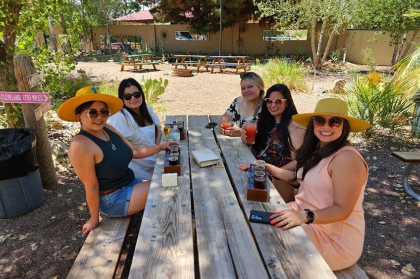 A group of people sitting at a wooden picnic table outdoors with a sign in the background. 1